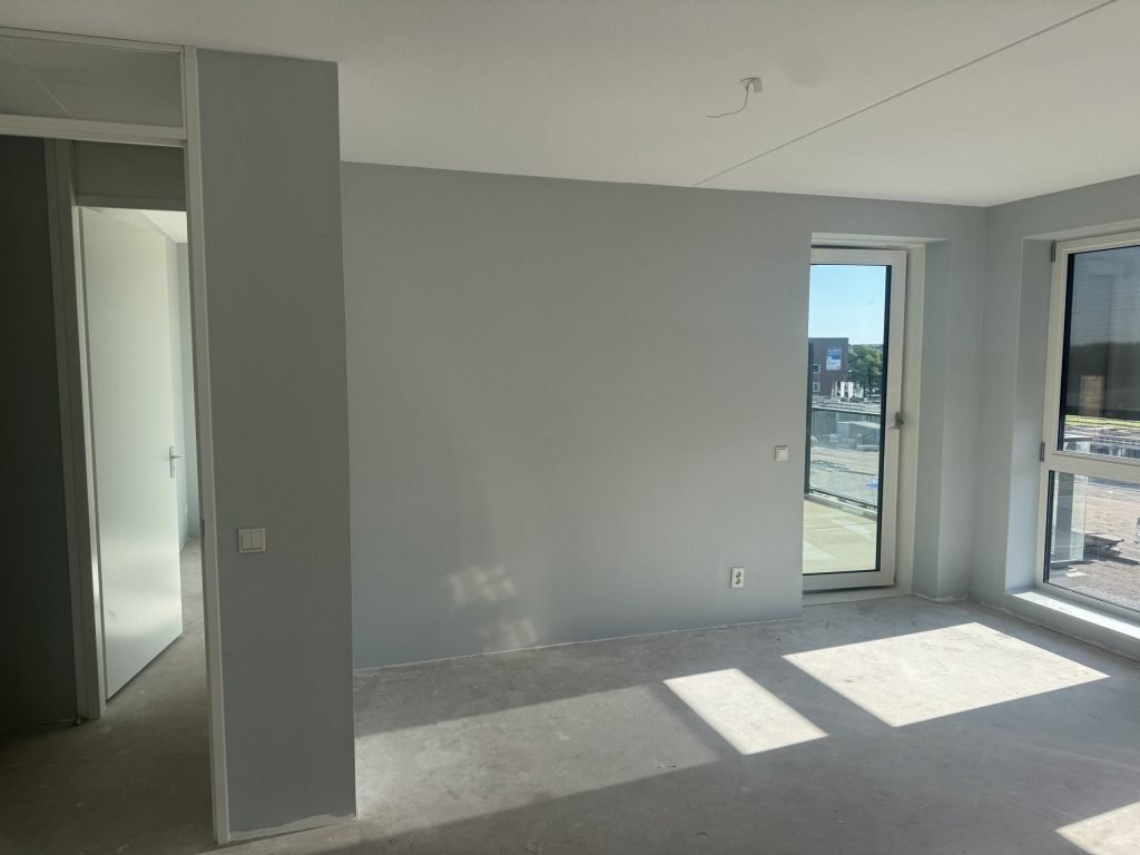 Lege nieuwbouwkamer met kale wanden en een betonvloer, kort na de sleuteloverdracht