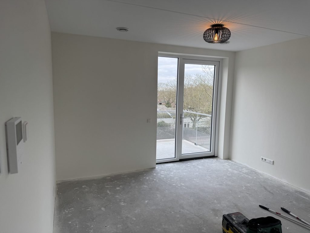 Lege kamer in een net opgeleverd huis met openslaande deuren naar het balkon en een kale betonvloer